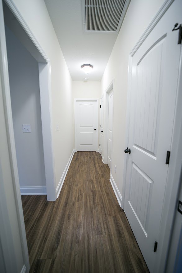 Hallway with white paneled doors, black door knobs, light wood flooring, and a floor vent