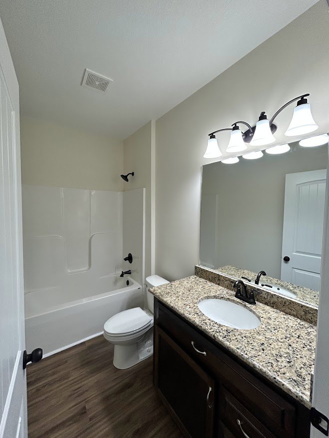 Bathroom with marble countertop, white toilet with lid down, row of light fixtures above mirror, wall vent, and tiled floor.