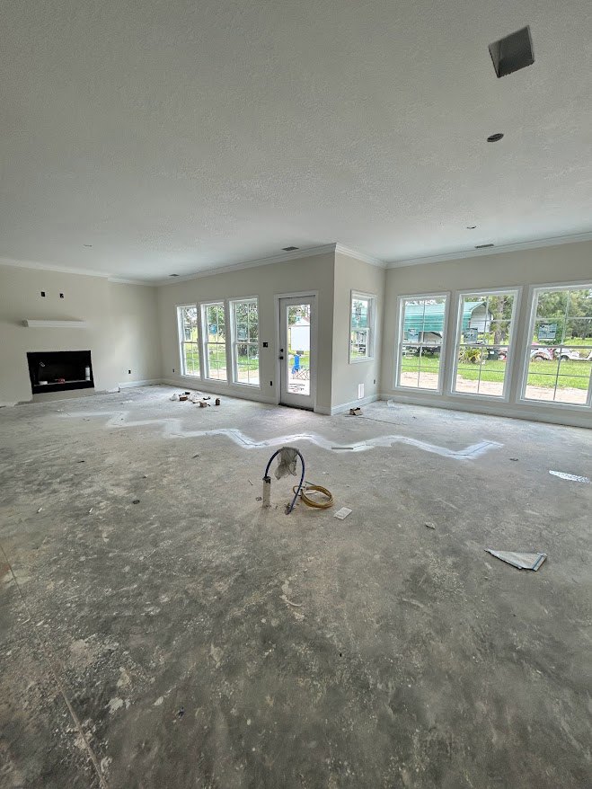 Concrete-floored room with plaster walls, large windows, white door, black shelf holding a white object, fireplace, and garden hose lying across the floor