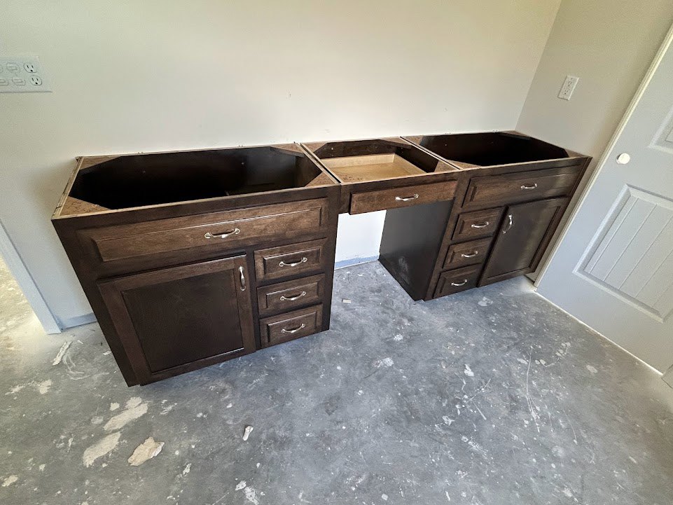 Light wood kitchen drawers beneath a white quartz countertop, set against a grey tile floor and white wall.