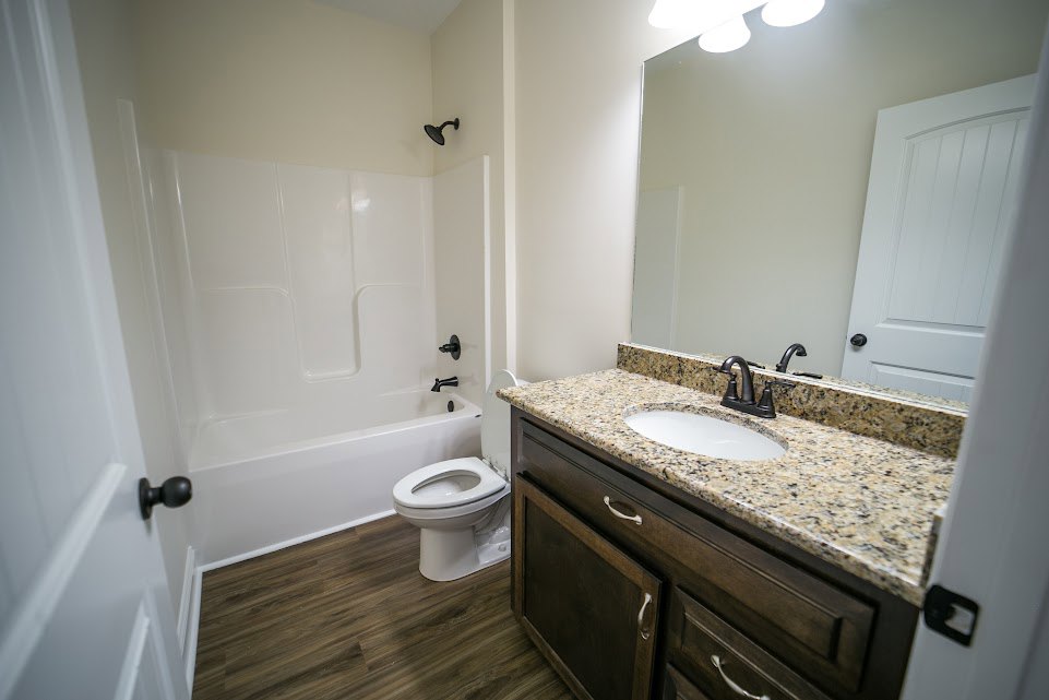 Bathroom with marble countertop, freestanding bathtub, white toilet, sink with chrome faucet, white paneled door, and light tile flooring