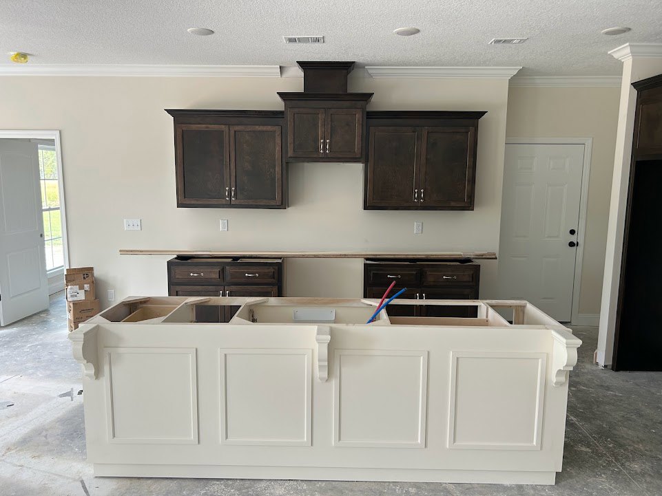 Modern kitchen featuring white cabinetry with black knobs, dark wood lower cabinets with silver handles, stone countertop, stainless steel sink, and built-in appliances.