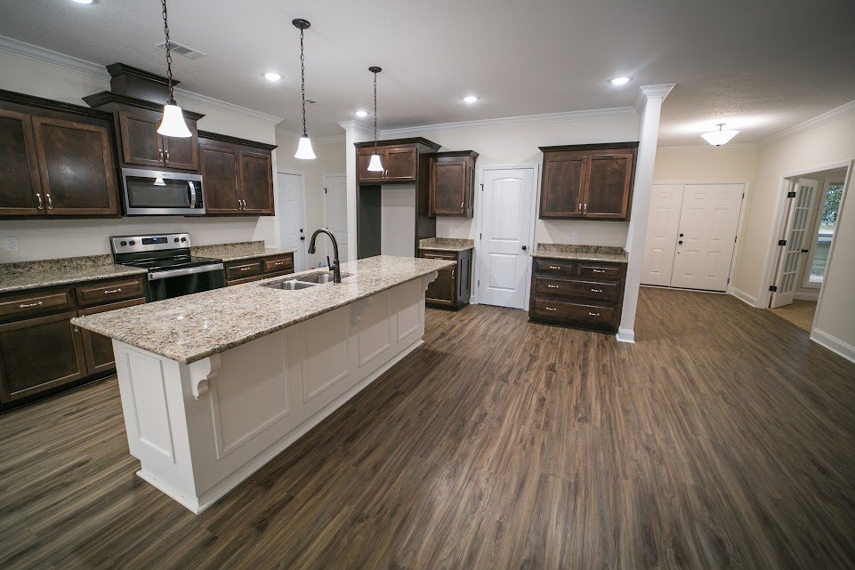 Open kitchen with wood flooring, white cabinetry with black handles, kitchen island featuring built-in sink and stove, stainless steel appliances including microwave under a
