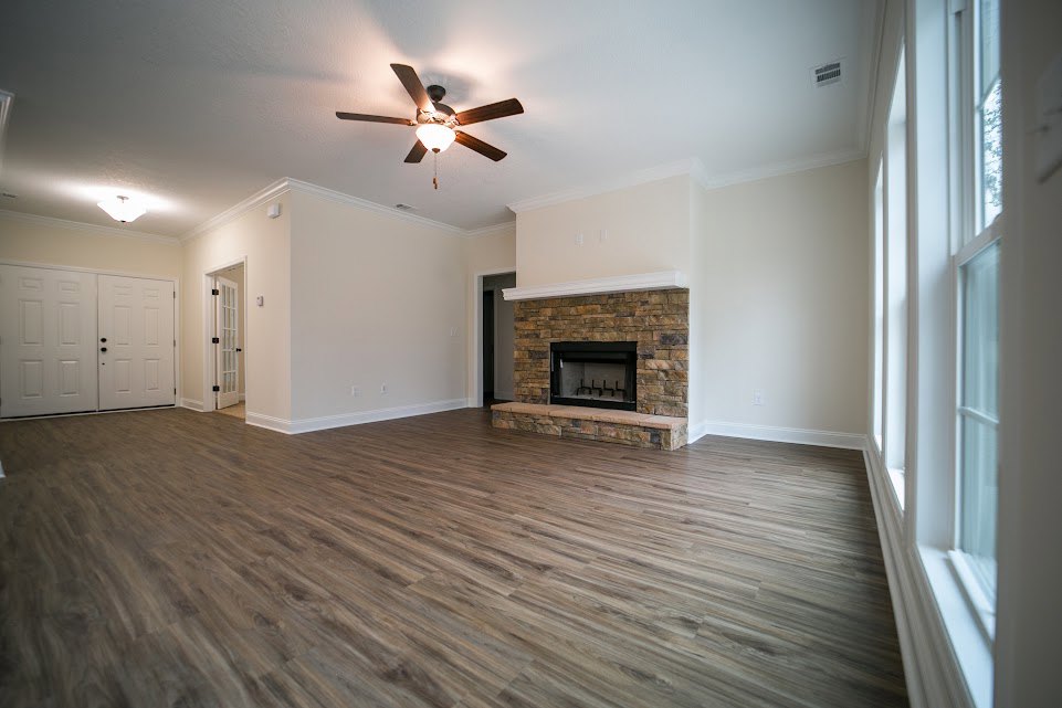 Living room with wood flooring, stone fireplace, ceiling fan with light, and white double doors with black knobs