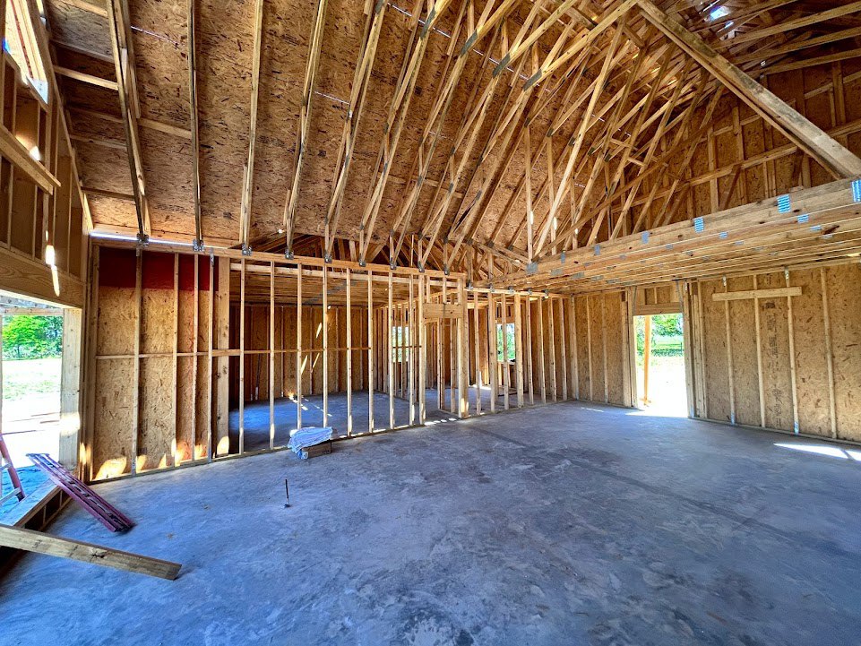 Unfinished room with exposed wooden ceiling beams, concrete floor, window, and construction ladder