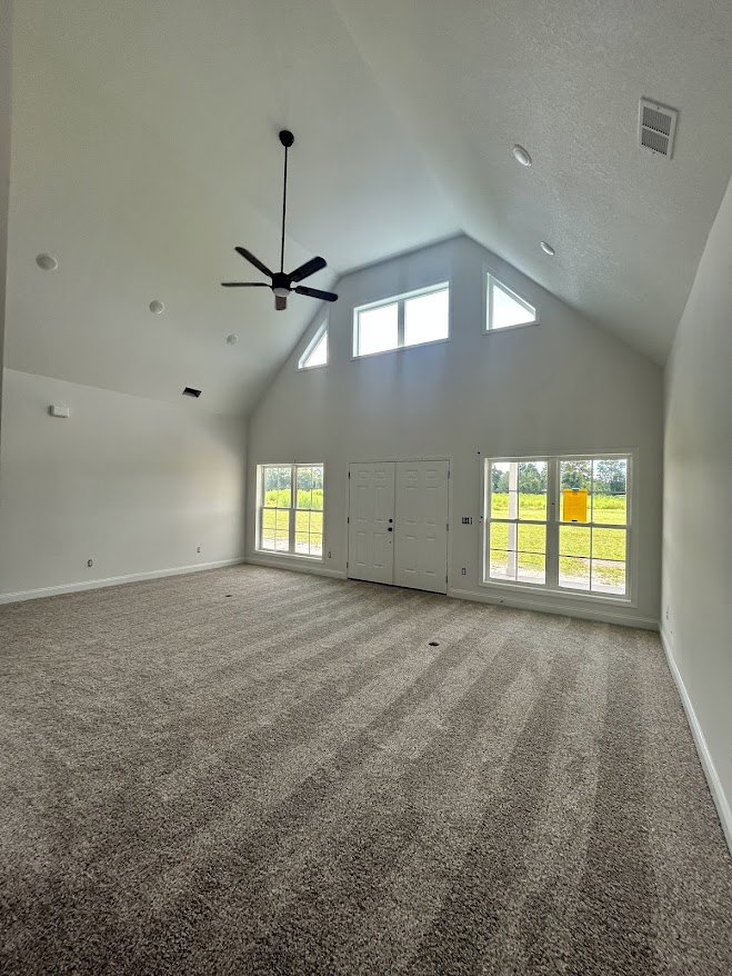 Ceiling fan with black handle mounted on white plaster ceiling, multiple windows with daylight streaming in, white double doors with black knobs, light-colored flooring
