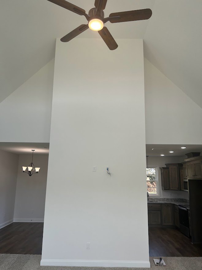 Ceiling fan with integrated light fixture mounted on white plaster ceiling, dark wood flooring below, white wall with light switch, black accent wall featuring central black