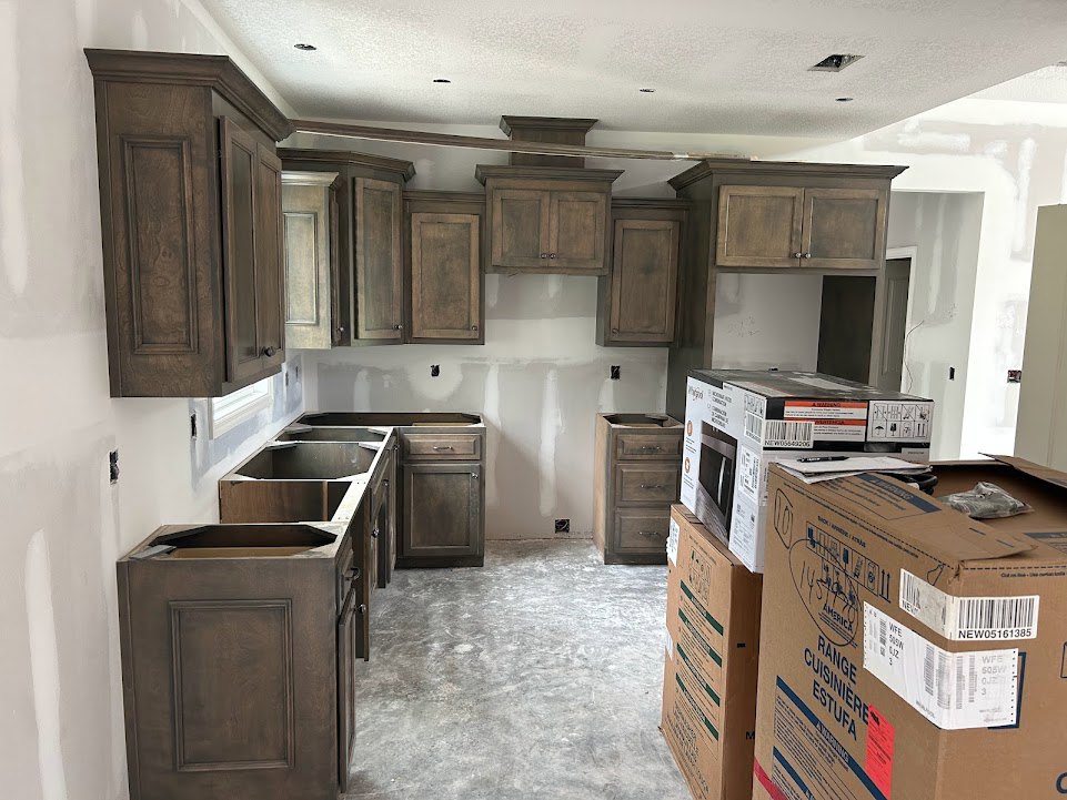 Kitchen with brown cabinets, cardboard moving boxes labeled green, visible drawer, and unfinished cabinet installation.
