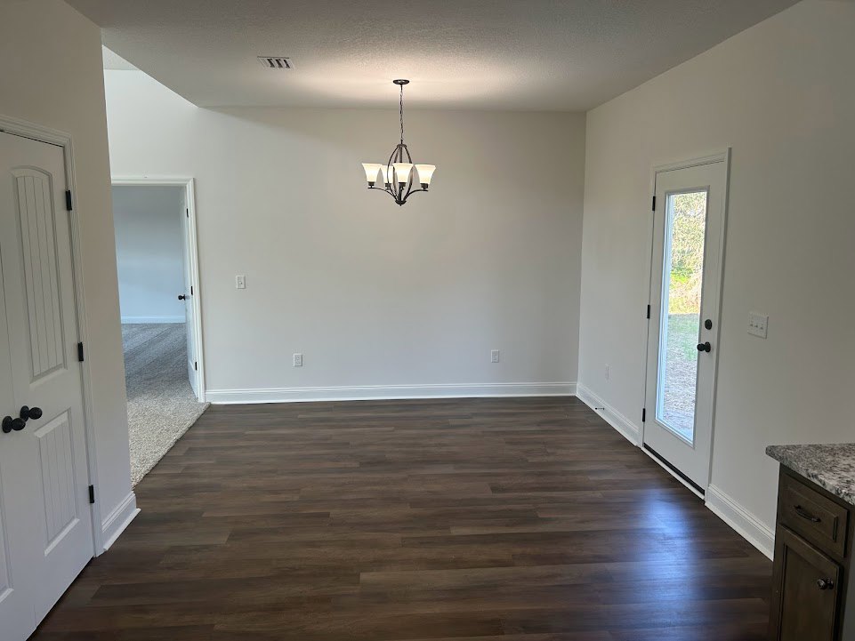 Wood flooring in a spacious room with a decorative chandelier, white door featuring black knobs and glass window, neutral plaster walls, and built-in drawers.