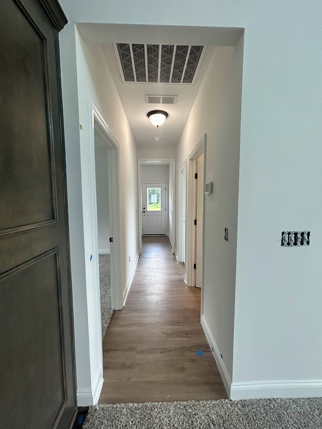 Hallway with white plaster walls, wood flooring, ceiling vent, and doors leading to adjacent rooms