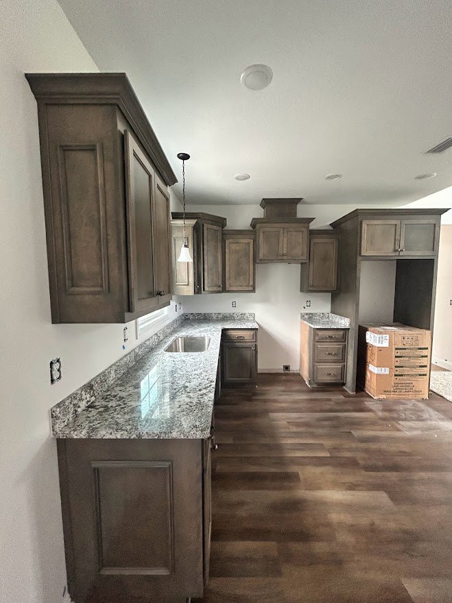 Kitchen with dark wood cabinets, granite countertops, stainless steel sink, and hardwood flooring; cardboard moving box sits on the floor near lower cabinetry.