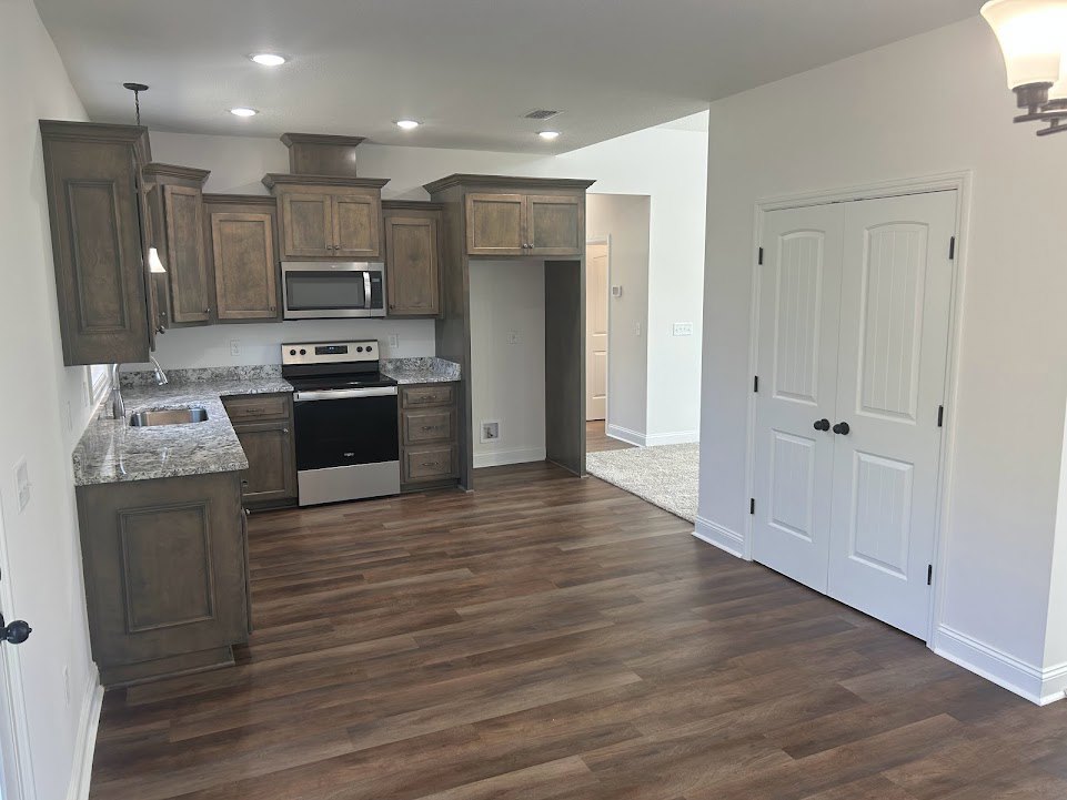 Kitchen with hardwood flooring, white cabinetry, black and silver stove, built-in microwave with digital screen, white door with black knobs, and a close-up of a modern lamp.