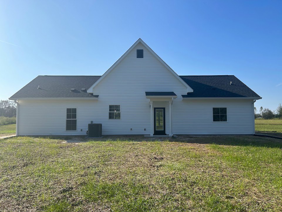White siding house with black front door, white-framed windows, and manicured green lawn under clear blue sky