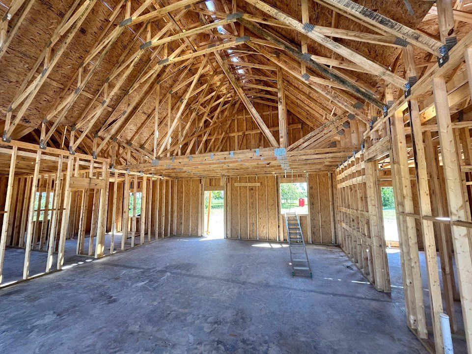 Exposed wood framing with ceiling beams, unfinished walls, and a ladder positioned near a window opening