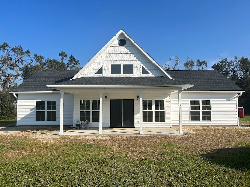 White siding house with black shingle roof, black framed windows with white trim, black front door, and manicured grass lawn