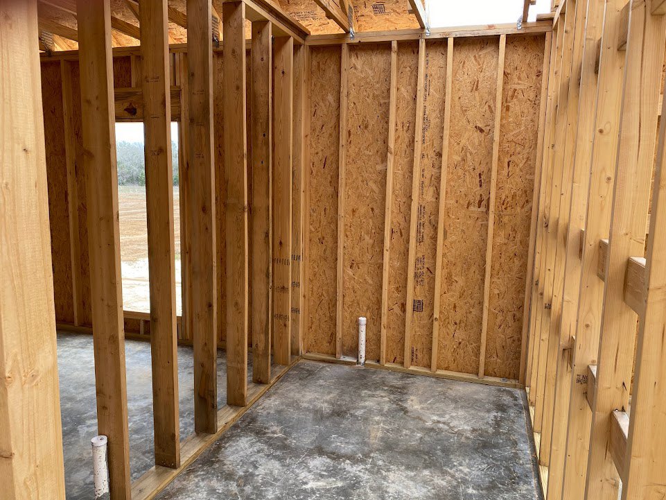 Open room with polished concrete floor, exposed wooden ceiling beams, and wood plank accent wall; outdoor wood fence visible through large windows.