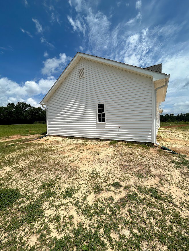 White siding house with large windows, surrounded by green grass lawn, blue sky with scattered clouds, and trees in the background