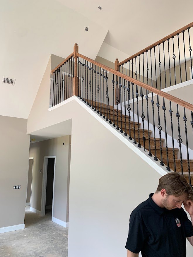 Man in black shirt sitting beside staircase with metal railings, black door frame visible, white walls and wood flooring in modern interior