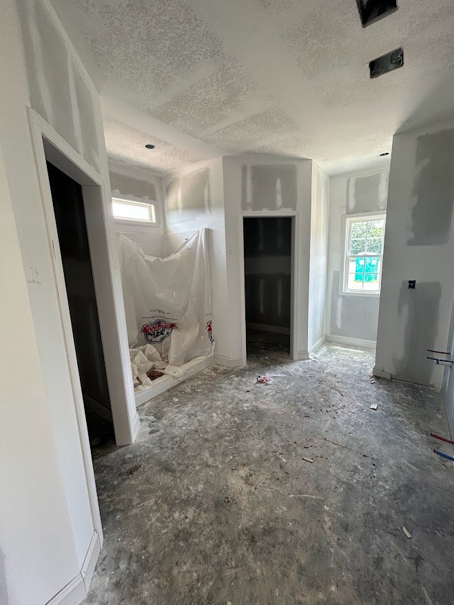 White-walled room with concrete floor painted white, window with blue door, white plastic bag featuring red and blue logos, black rectangular object on white surface, and black
