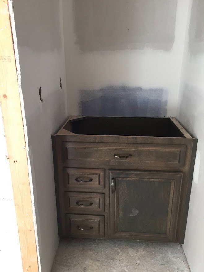 Wooden cabinet with brushed metal handles and multiple drawers, set against a light-colored wall, white carpet with black border visible in foreground