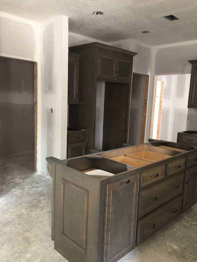 Modern kitchen featuring a central island with grey countertop and wooden frame, white cabinetry against a white wall, and drawers with sleek hardware