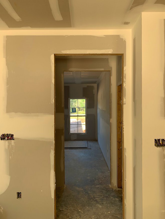 Hallway with white plaster walls, open doorway, window with sign, light wood floor, and ceiling fixture
