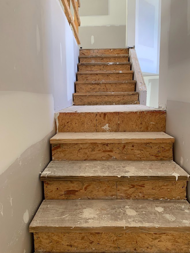 Wood staircase with matching wood flooring, white walls, and minimalist handrail.