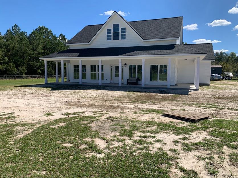 White house with black roof, expansive grassy yard, white gazebo, multiple windows, trees in background, partly cloudy sky