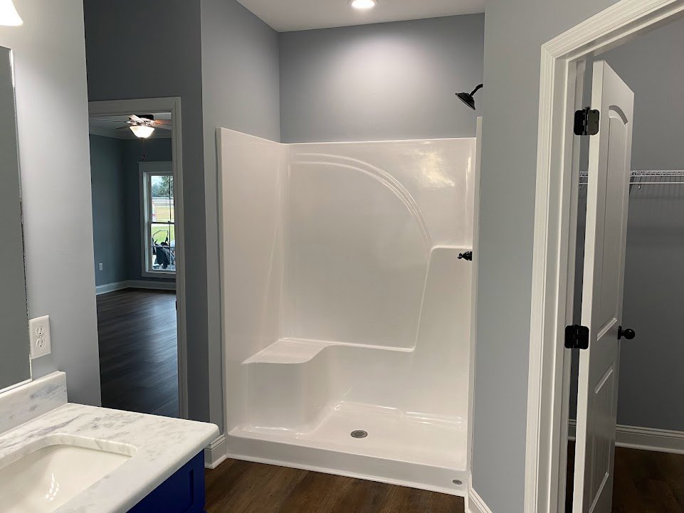 Bathroom with white shower stall featuring a step and drain, white sink set in marble countertop, black wood floor, and white door with black handle