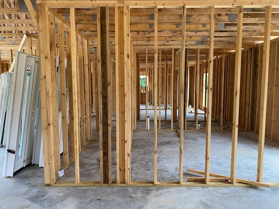 Exposed wood framing and beams with unfinished concrete floor, window opening, and wooden shelf in a residential interior under construction