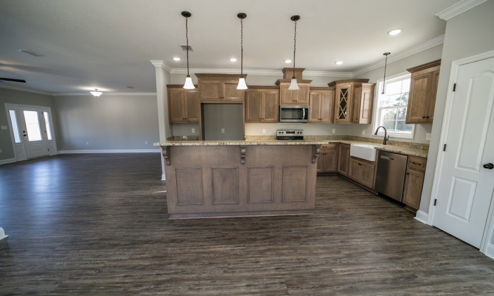 Kitchen with wood flooring, central island featuring brown wooden countertop, white cabinetry, white door with black handle and three windows, white walls with light switch