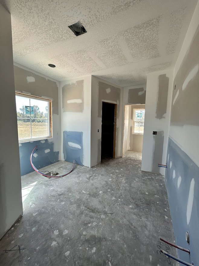 Modern interior room with plaster walls, composite flooring, open door, large window with sign, exposed circular pipe, and plastic container holding a white item.