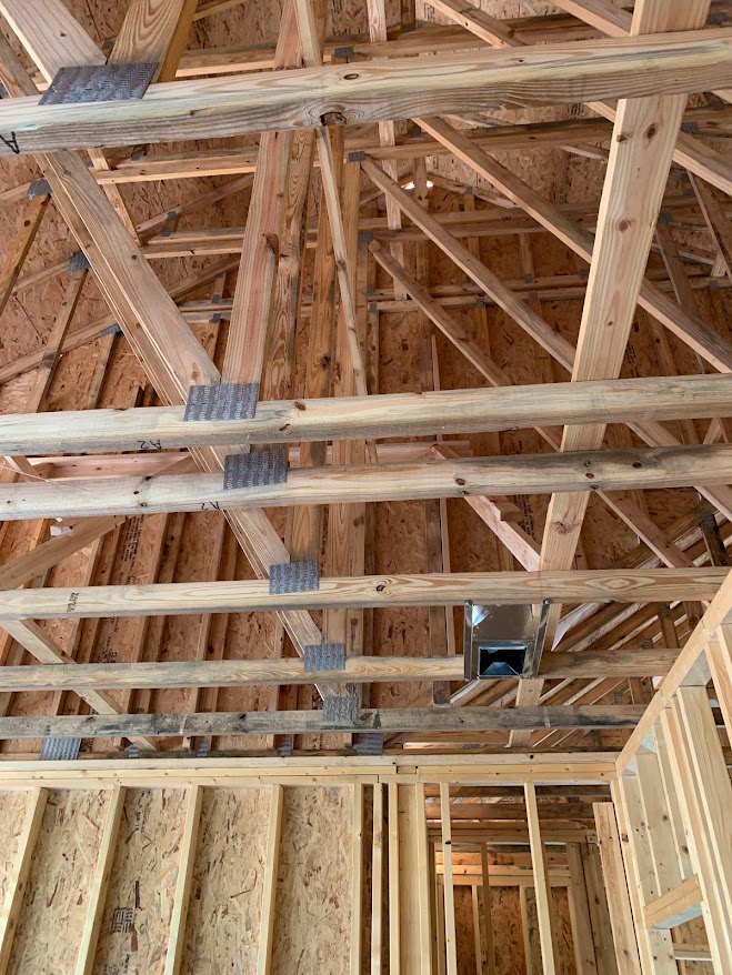 Exposed wood framing and beams with metal pipes and building insulation inside a partially constructed residential home