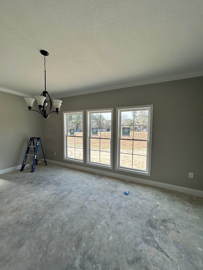 Open room with concrete floor, plaster walls, ladder leaning against wall, row of large windows overlooking grassy field, chandelier hanging from ceiling, window with sign attached