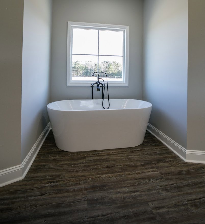 Freestanding white bathtub with black faucet on wood floor, large window, bicycle, and industrial-style black lamp in modern bathroom