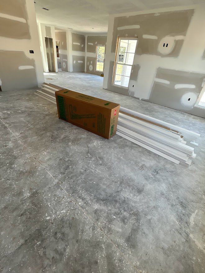 Open room with white ceiling beams, brown box on light flooring, window with central mullion, white molding, and white sink featuring black lines