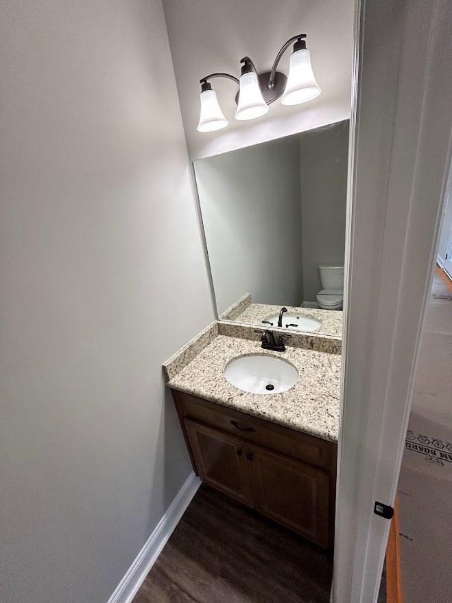 Bathroom with marble countertop, rectangular mirror above sink, black faucet, white cabinetry, and tiled wall.