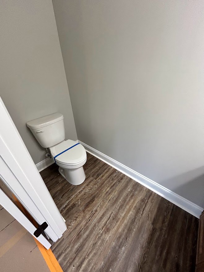 White toilet with blue band against plaster wall, laminate wood flooring, and white finishes in residential bathroom