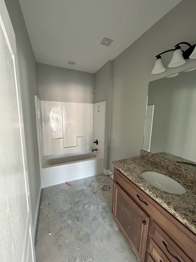 White oval sink set in a marble countertop beside a glass-enclosed shower, with tile walls and modern cabinetry.