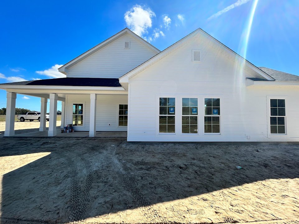 White two-story house with multiple square windows, tire tracks in sandy ground, blue sky with scattered clouds, porch area, blue signs visible in some windows