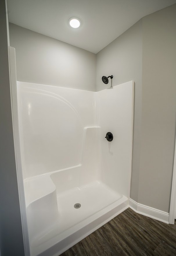 White tile shower with glass door, chrome fixtures, and wood floor with white baseboard in modern bathroom