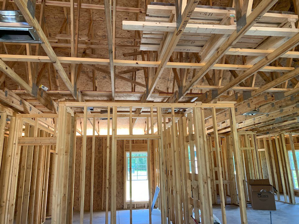 Exposed wooden beams and framing inside a partially constructed house, with visible lumber, ceiling structure, and building insulation.