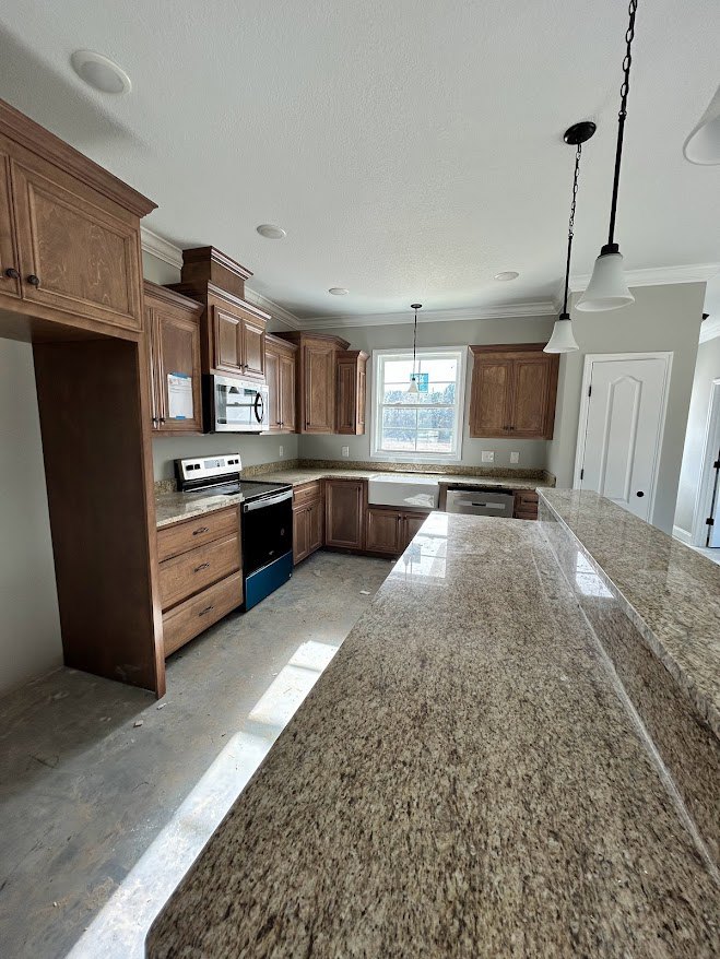 Marble countertop kitchen with white cabinetry, stainless steel sink, built-in microwave, pendant ceiling light, and light wood flooring