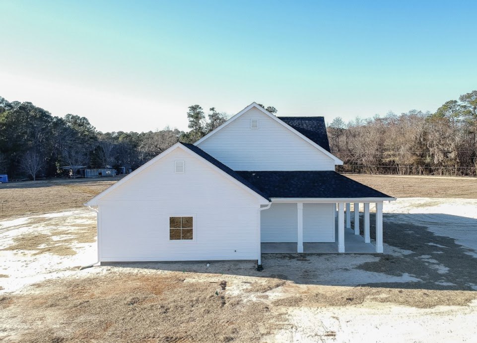 White house under construction with black roof, square window, surrounded by open field and blue sky