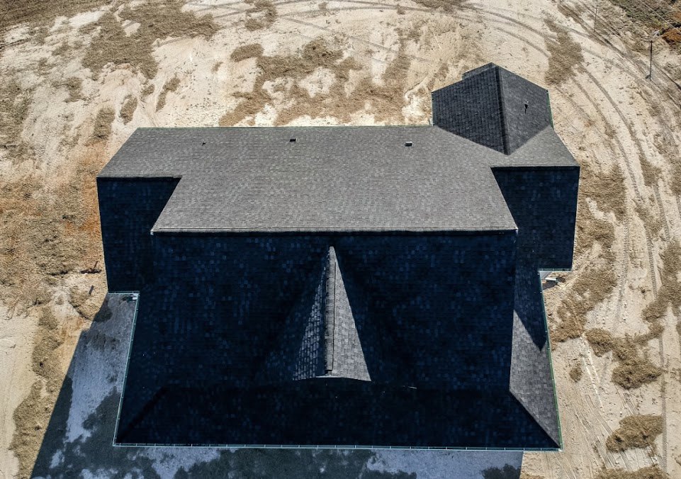 Modern black square house with flat roof, central skylight, and minimalist exterior surrounded by gravel landscaping