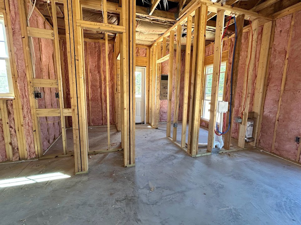 Unfinished room with exposed wood framing, concrete floor, door with window, construction light, and white electrical box with labels