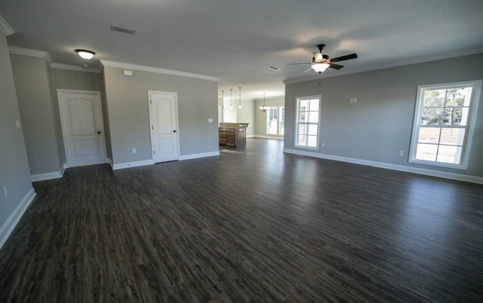 Spacious room with hardwood flooring, wood ceiling fan, white-framed window offering outdoor view, white door with black hardware, and a countertop along one wall