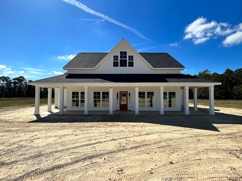 White house with tall white columns, red front door, triangular roof, tire tracks in sandy driveway, blue sky, close-up of window, trees in background
