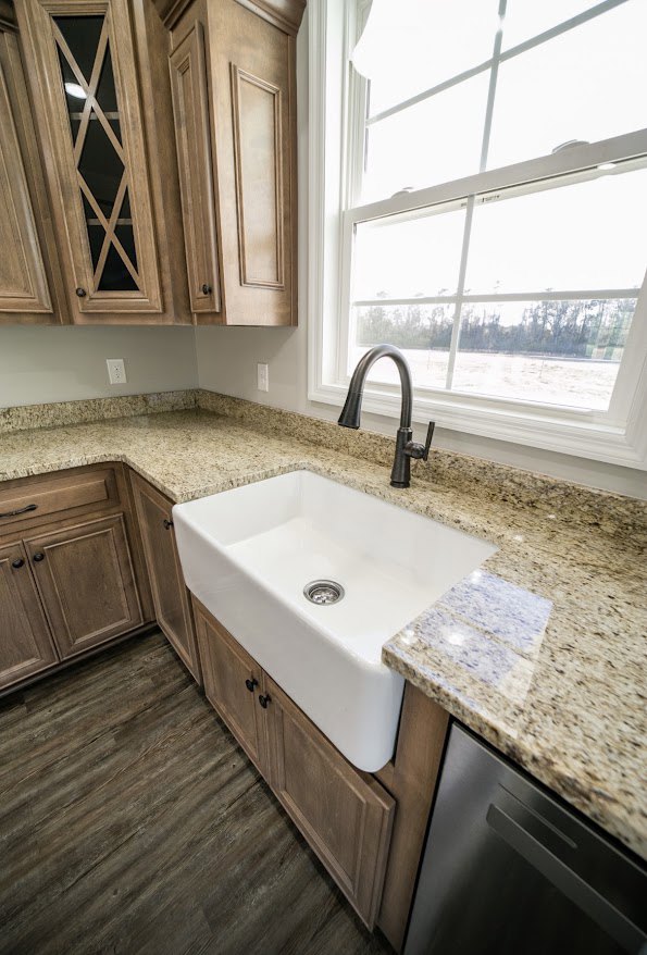 Granite countertops with a white undermount sink, chrome faucet, wood flooring, white cabinetry, and a window overlooking a grassy field