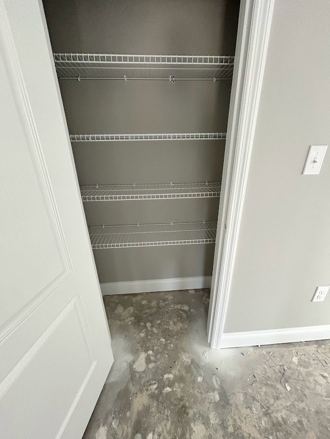 White closet with built-in shelves, light switch on adjacent wall, open door, and unfinished floor with scattered debris.